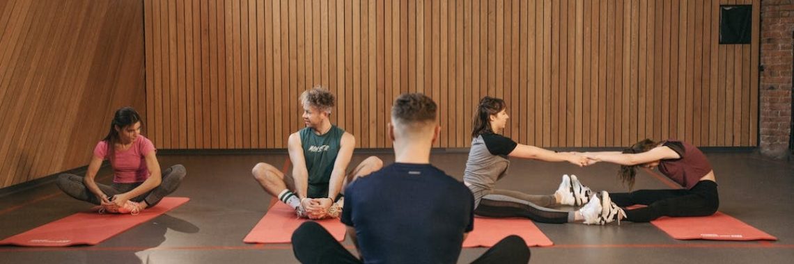 A group of adults practicing yoga and stretching on mats in a wooden panelled room.